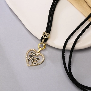 Macro detail of a gold heart pendant with black Fé engraving and small diamonds on a black cord