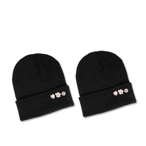 Two black knitted beanies featuring decorative heart, flower, and rhinestone snow brooches