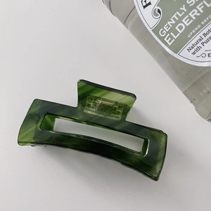 Close-up of a dark green acetate hair claw clip with a marble texture on a white surface