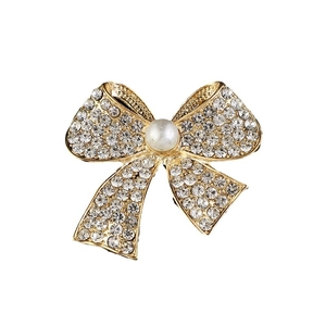 Broche nœud dorée avec strass scintillants et une perle centrale sur fond blanc immaculé
