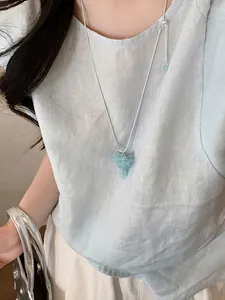 Primo piano di una collana d'argento con pendente a forma di uva blu chiaro su una modella
