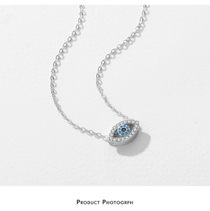 Macro shot of silver Evil Eye necklace with blue and clear pavé crystals on a white base