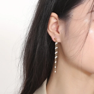 Detail of long gold tassel earrings with white enamel beads on a female model