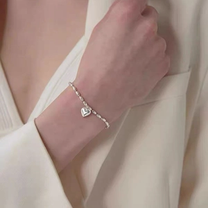 Detailed view of silver heart pendant bracelet on wrist with elegant rice bead chain