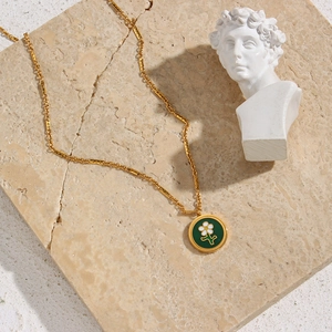 Detail of 18K gold plated necklace with green flower pendant on a stone pedestal