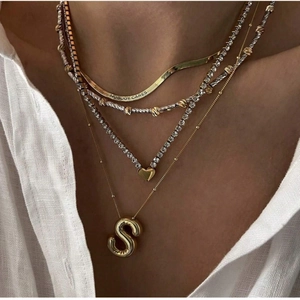 Close-up of gold balloon S letter pendant layered with engraved choker and heart charm
