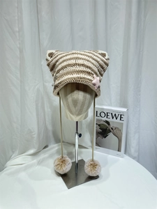 Detail of knit cat ear hat with striped pattern, pink star patch and fluffy pompom ties
