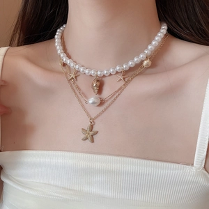 Macro shot of layered necklace featuring gold starfish, conch charms and baroque pearls