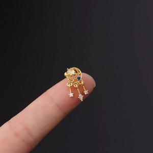 Gold moon stud earring with colorful zircon stones and dangling charms held on a fingertip