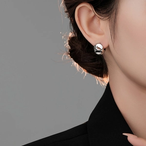 Close-up of minimalist irregular silver ball hoop earring worn on a model with black suit