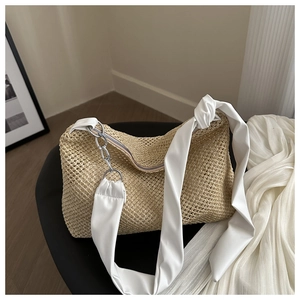 Close-up of beige woven straw shoulder bag with white fabric strap and silver chain detail