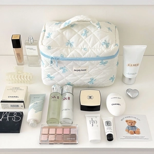 Quilted white toiletry bag with blue bow prints and various cosmetics on a white surface