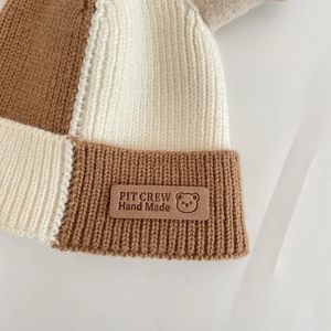 Détail du bonnet en maille color block montrant le patch en cuir fait main et texture