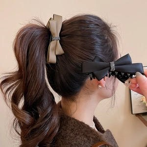 Detail showing oversized satin bow hair claw clips with rhinestones on wavy brown hair