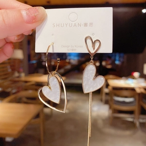 Macro detail of asymmetric gold heart tassel earrings with marble texture on display card