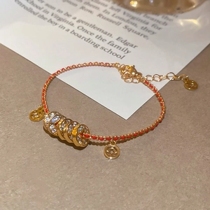 Vue macro d'un bracelet en corde rouge tressée dorée avec pièces et perles de zircon