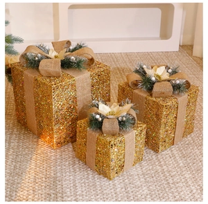 Detail of three beige Christmas gift boxes with gold glitter, burlap bows and pine needles