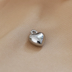 Macro shot of silver heart pendant with high gloss finish on beige fabric texture