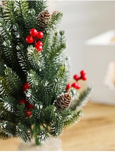 Close-up of mini snow-flocked Christmas tree with red berries and burlap base