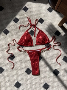 Detail of red metallic bikini with pearl accents and shiny fabric on a textured rug
