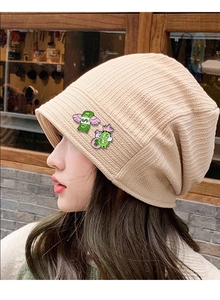 Detail view of cartoon enamel pins on a beige knitted beanie with winged dollar design