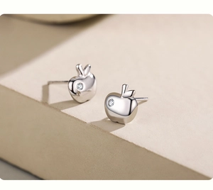 Macro shot of silver apple stud earrings with a tiny zircon on a beige pedestal