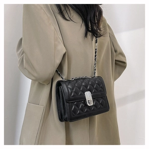 Detail of black quilted chain bag with silver twist lock on a beige blazer outfit