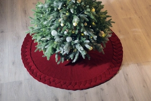 Detailed knit texture of dark red Christmas tree skirt with braided border on wood floor