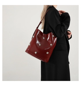 Close-up of stylish reddish-brown glossy tote bag featuring large silver metal studs