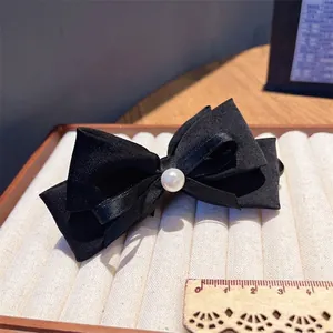 Detail of black satin bow hair clip with center pearl on a velvet display tray