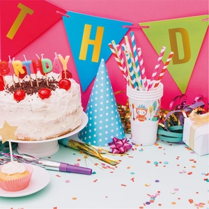 Close-up of rainbow party set including birthday candles, paper hats and banners