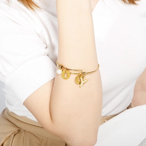 Detail of adjustable gold bangle with Y-letter charm, pearl and silhouette pendant