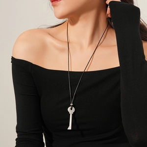 Gros plan d'un pendentif clé argenté sur une longue chaîne porté sur un pull noir