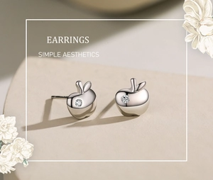 Macro detail of apple-shaped silver earrings featuring centered white diamond inlay