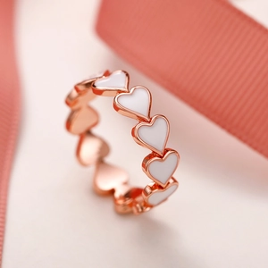 Vue détaillée d'une bague en or rose avec des cœurs en émail blanc interconnectés