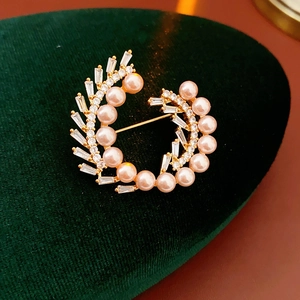 Macro detail of a gold-plated wreath brooch featuring pink pearls and cubic zirconia