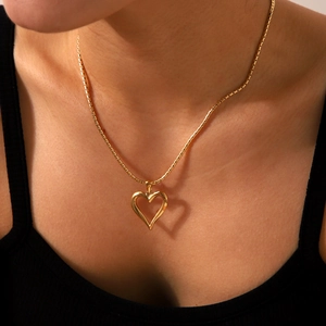 Close-up of a gold hollow heart pendant necklace worn on neck with metallic luster