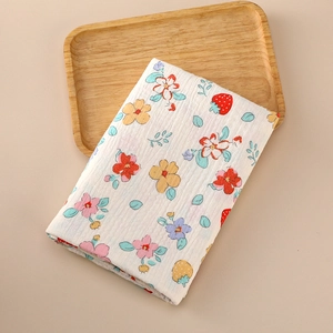 Detail view of a soft cotton muslin baby wrap featuring strawberry and floral print patterns