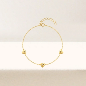 Detail of gold heart charms with starburst engravings and clear gemstones on a dainty chain