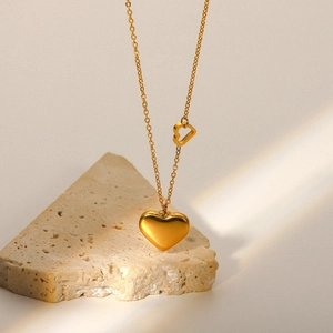 Detailed close-up of 18K gold-plated double heart pendant necklace on textured stone