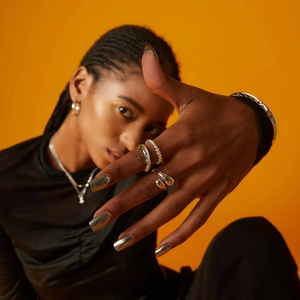 Close-up of silver stainless steel teardrop rings and bracelets on bright orange background