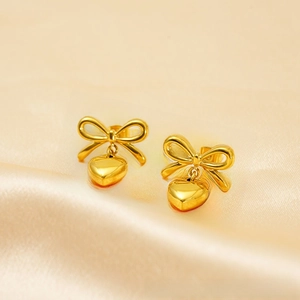 Macro detail of gold bow and heart drop earrings on champagne satin background