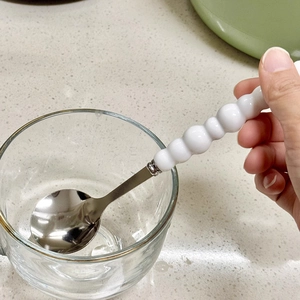Polished stainless steel spoon with white beaded creative handle shown in a hand