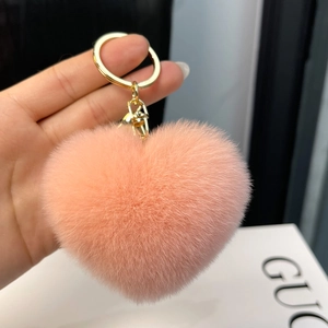 Close-up of heart-shaped fluffy rabbit fur keychain in coral pink with gold metal clasp