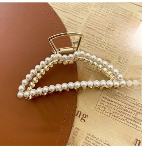 Detail of a gold metal hair claw clip with white pearls on vintage newspaper background