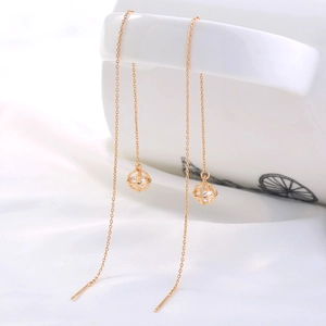 Detail view of a long gold chain earring with a hollow sphere and a sparkling zircon stone
