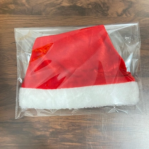 Red velvet Christmas hat with white plush trim in transparent protective packaging