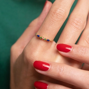 Detailed close-up of a slender gold ring with colorful gemstones on a model finger