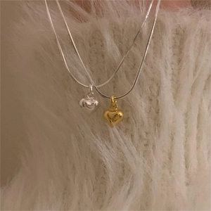 Minimalist heart pendant necklace with gold and silver snake chains on soft white knit