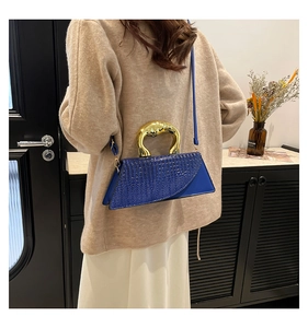 Detail of blue crocodile pattern handbag featuring a luxury gold metal top handle